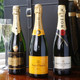 The Sparkles. Three bottles of champagne are displayed on a wooden surface. The first bottle is from Bernard Remy Champagne, the second is Veuve Clicquot Brut with a distinctive yellow label, and the third is Moët & Chandon Imperial. In the background, there are two champagne flutes beside the bottles. The Sparkles. Three bottles of champagne are displayed on a wooden surface. The first bottle is from Bernard Remy Champagne, the second is Veuve Clicquot Brut with a distinctive yellow label, and the third is Moët & Chandon Imperial. In the background, there are two champagne flutes beside the bottles.
